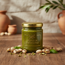 Laden Sie das Bild in den Galerie-Viewer, Feinkost Ranieri Pesto Pistazien aus Sizilien in Glas mit goldfarbenem Deckel, frische Pistazien liegen auf einem rustikalen Holztablett
